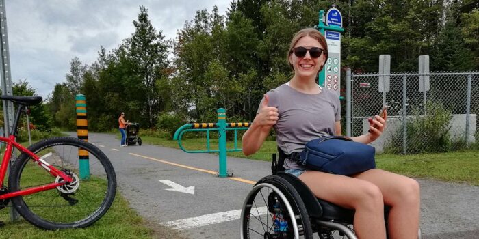 Woman using a wheelchair gives a thumbs up on an accessible trail