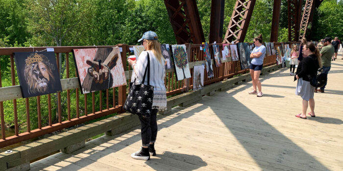 Art being displayed on the Bill Thorpe Walking Bridge with onlookers walking by