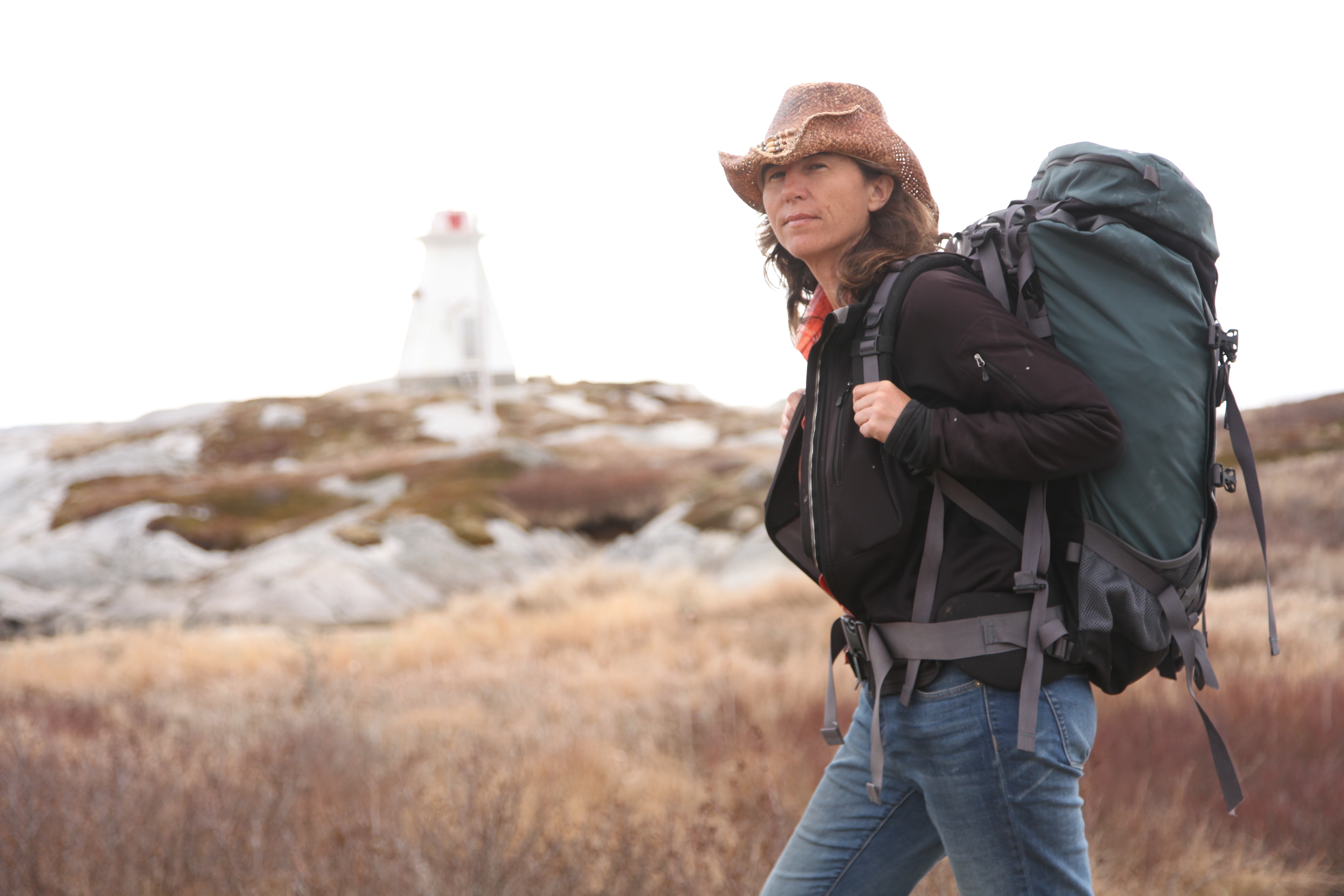 Dianne Whelan walks by a lighthouse with backpack on.