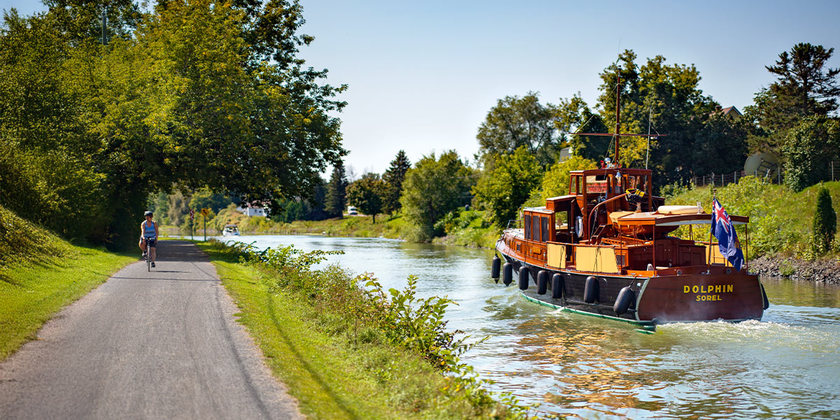 A serene boat gliding along the tranquil waters of the Richelieu River, surrounded by lush greenery. Un bateau serein glissant sur les eaux tranquilles de la rivière Richelieu, entouré d’une végétation luxuriante.