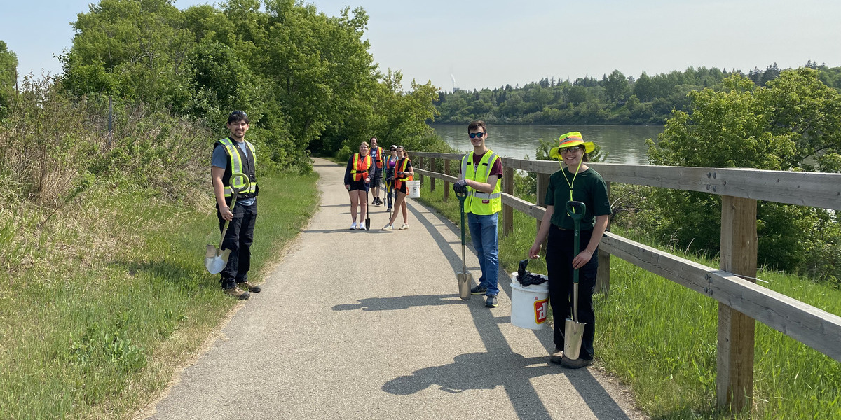 people standing in construction gear with shovels posing for photo on a trail on sunny day