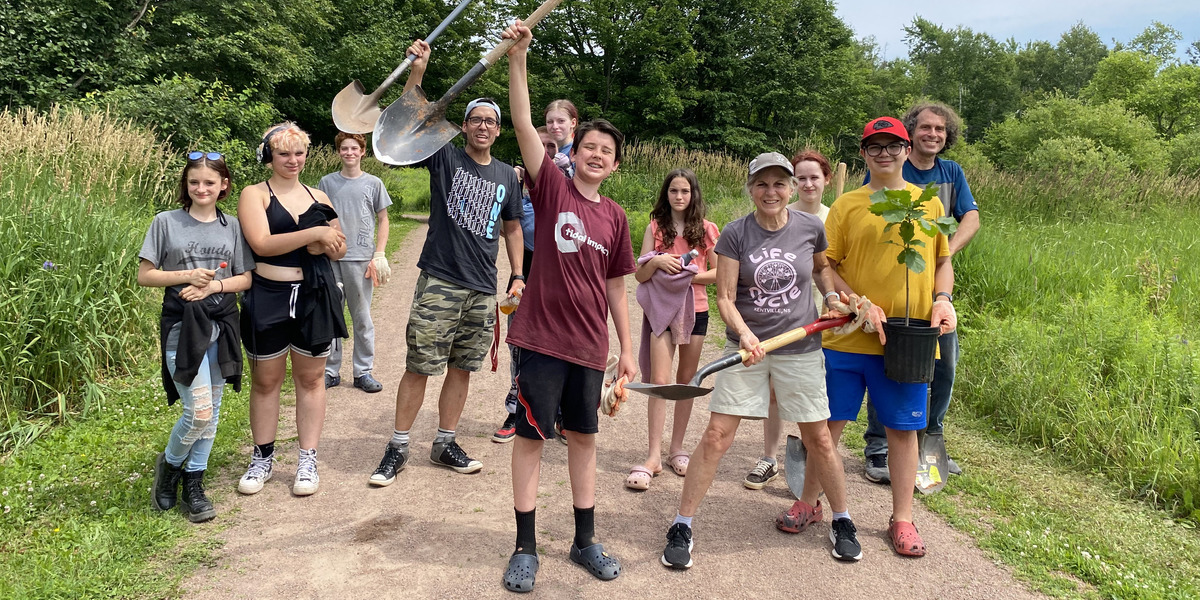 people standing in a group with shovels in the forest smiling for a photo