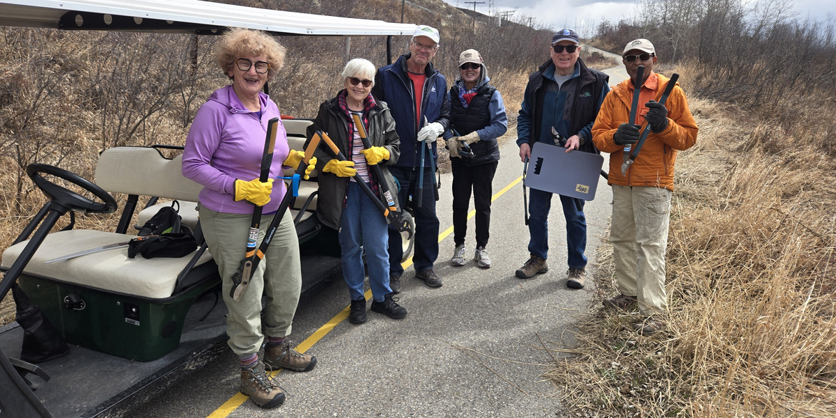 people smiling holding hedge trimmers on a paved road