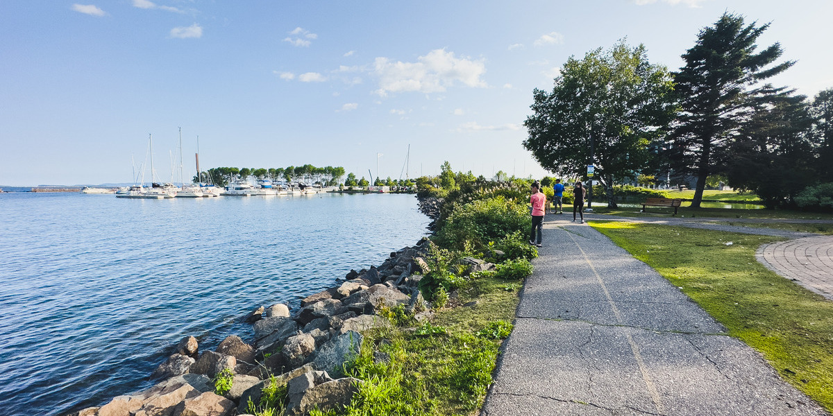 ON - City of Thunder Bay - July 2023 | Trans Canada Trail people walking on bike trail on sunny day with water alongside