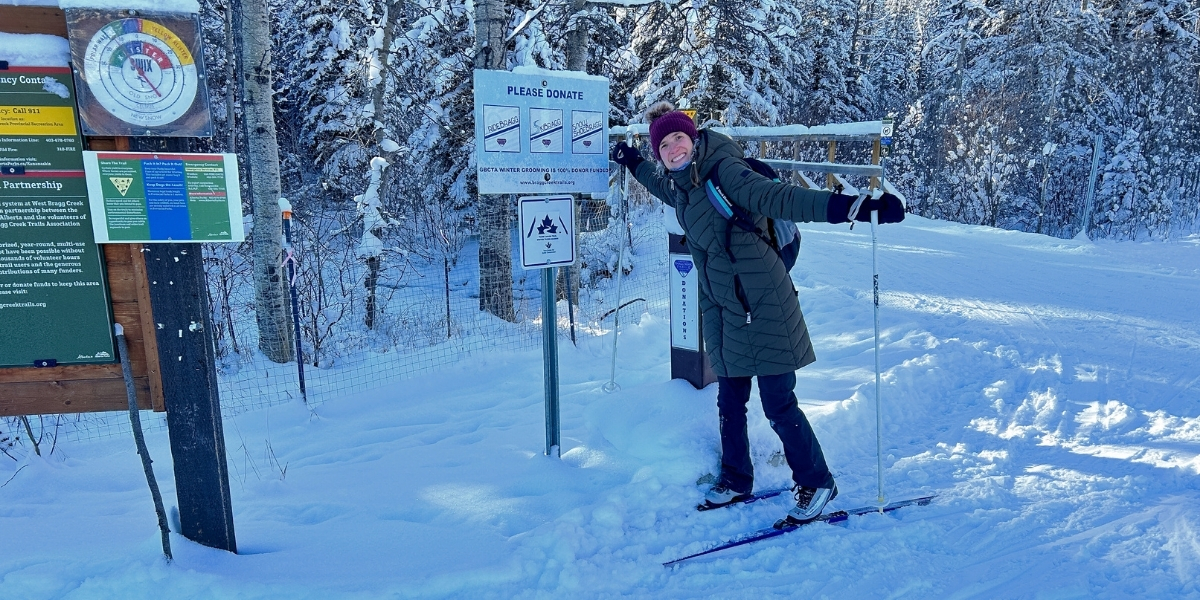 woman smiling on skis in the snow pointing to a sign