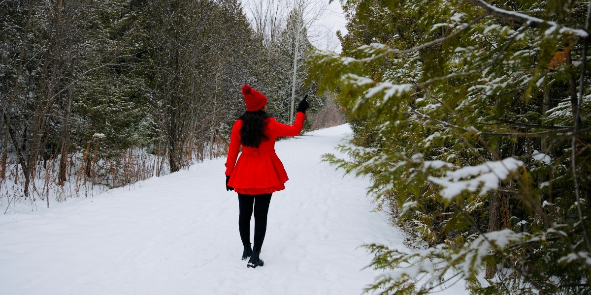 woman in red dress walking on a snow covered trail in forest