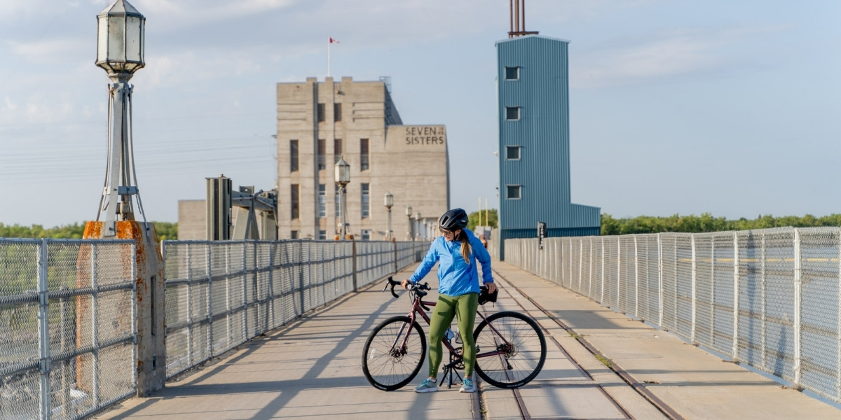 woman on bike on paved bridge with large building behind