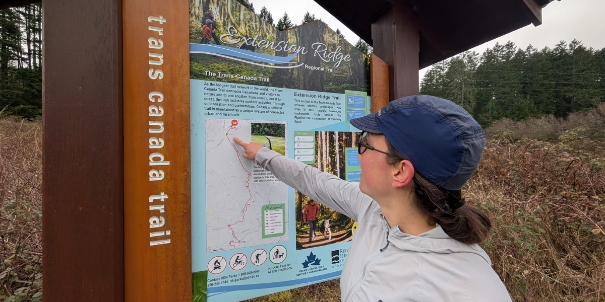 person pointing at a large trail map in a meadow