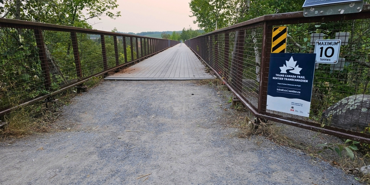 large bridge with trail signage looking toward cloudy sunset