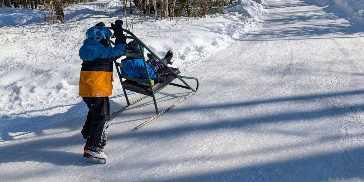 person pushing a child on a skating sled on ice trail