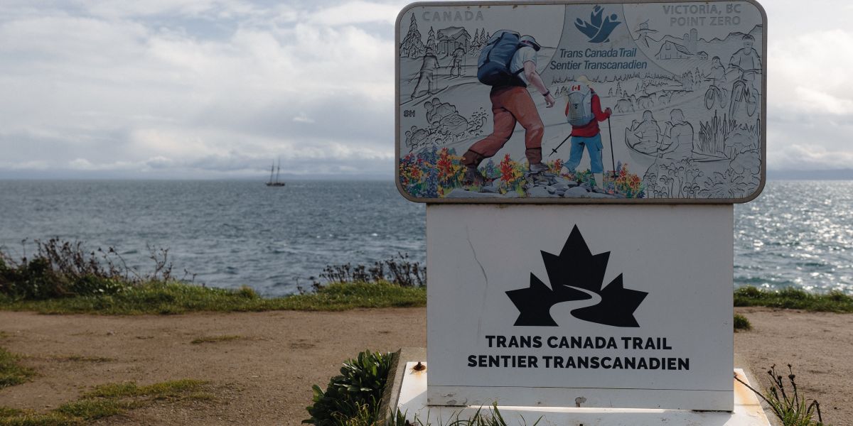 signage on a trail of man and boy hiking with water behind
