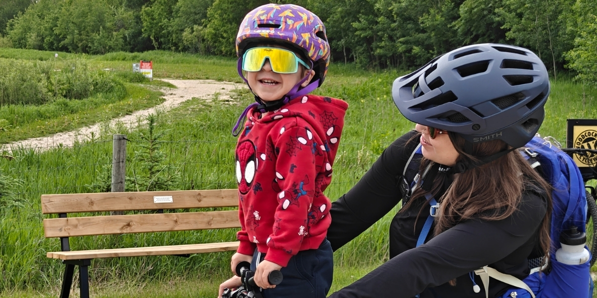 woman and child on a bike with child smiling in sunglasses in grassy area