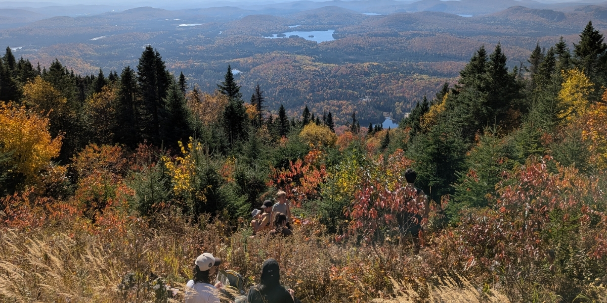 two people sitting at hike lookout over fall foliage and lakes below
