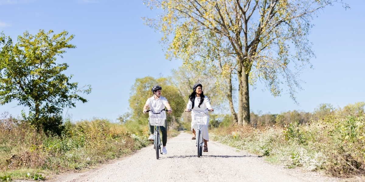 two people riding a bike on a paved trail on a sunny day