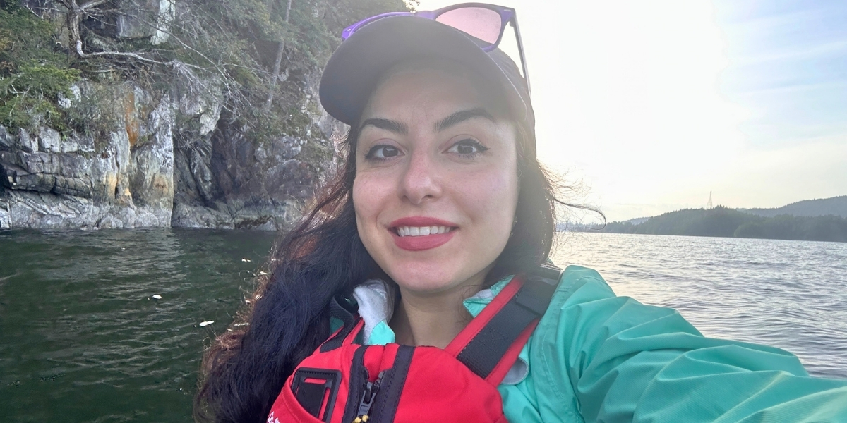 00Feature image_GCH_Fate M_credit Fate Mayanloo | Trans Canada Trail Smiling woman in a red life jacket and teal jacket taking a selfie on a lake, with rocky cliffs and trees in the background.